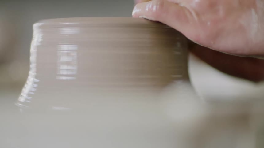 A white woman shapes clay into pottery