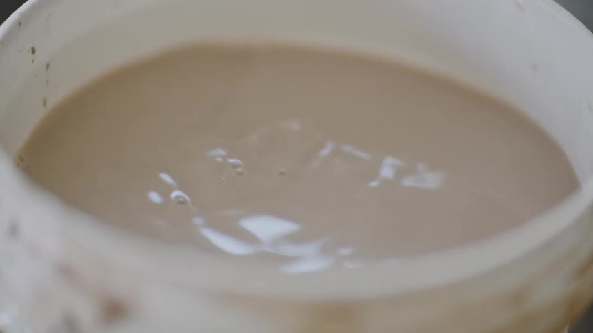 Closeup on a bucket and a female hand placing a piece of clay in the bucket with water