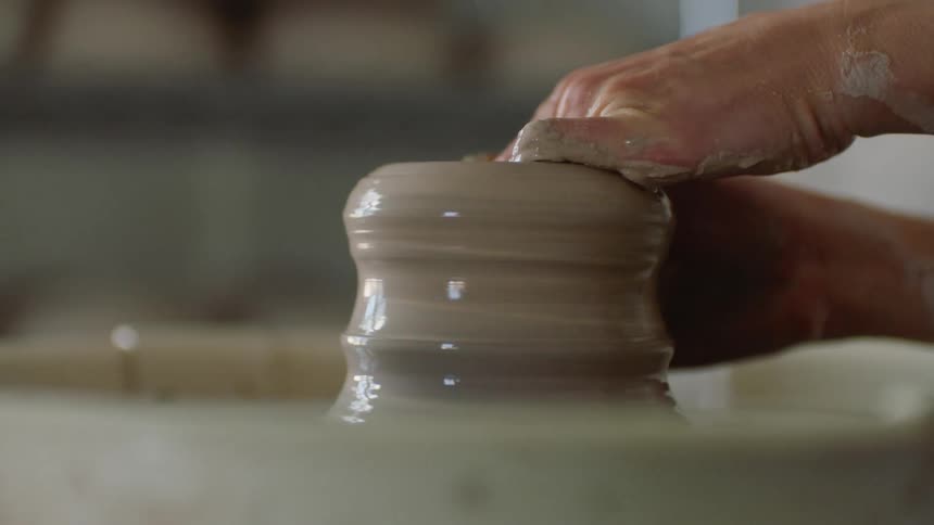 Hands of a woman sculpting a vase with clay