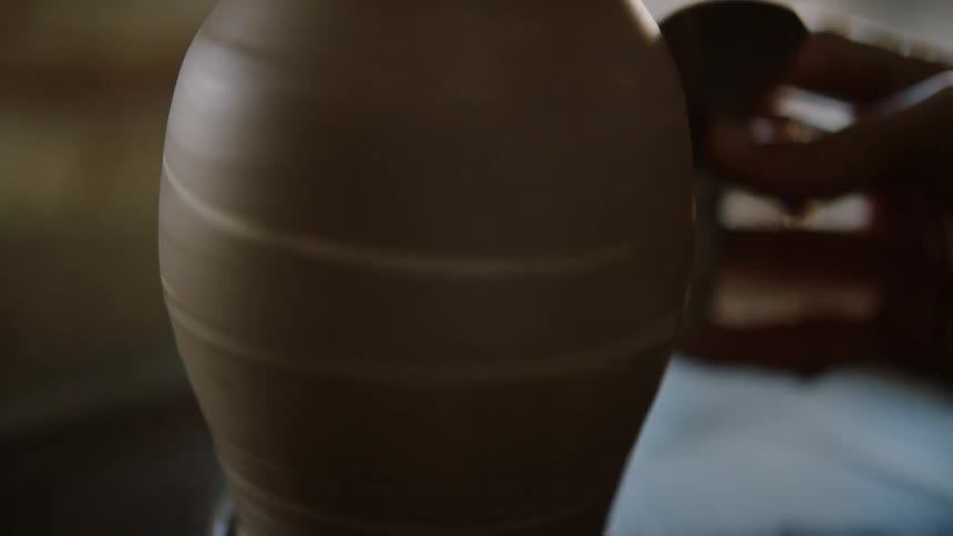 A person is sculpting a clay jug while it is spinning