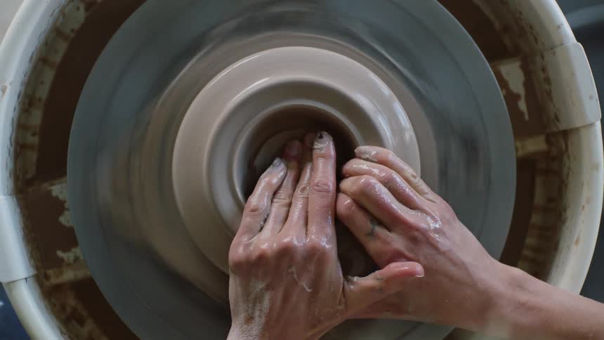 Hands of someone making bowl on a sculpting wheel