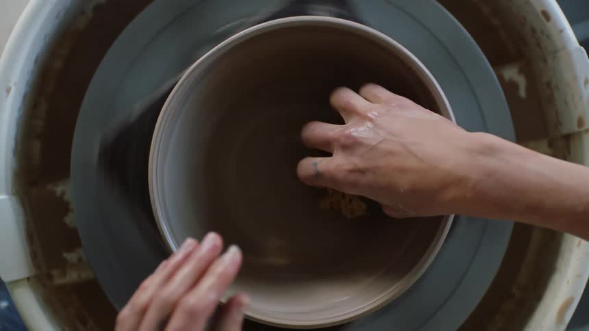 A person modeling a clay bowl with a sponge
