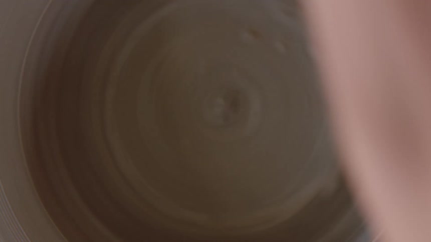 Female potter shapes clay turning on wheel into a shallow dish