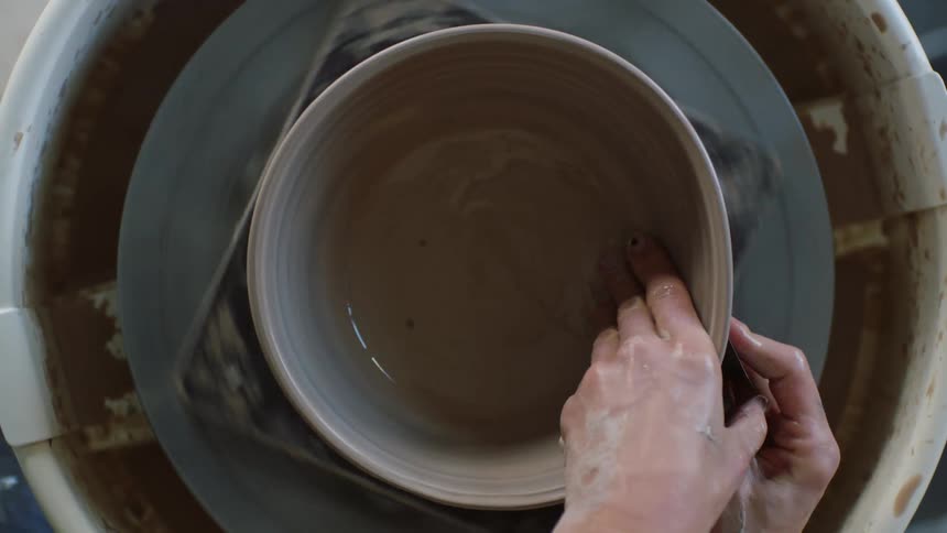 A human hand is modeling clay that is swirling on a round plate