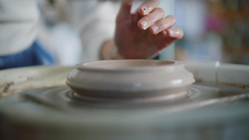 A woman shapes a wet piece of clay that is spinning on a pottery wheel