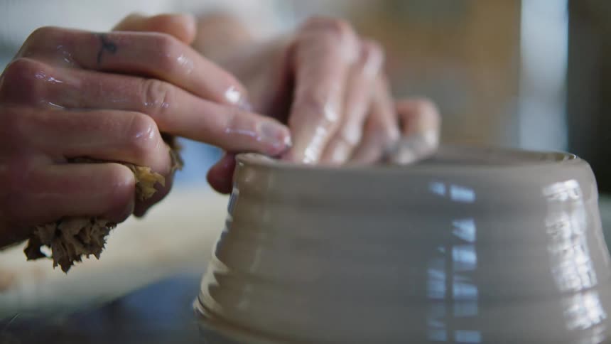 A woman carefully keeps shapes a piece of clay spinning on a pottery wheel