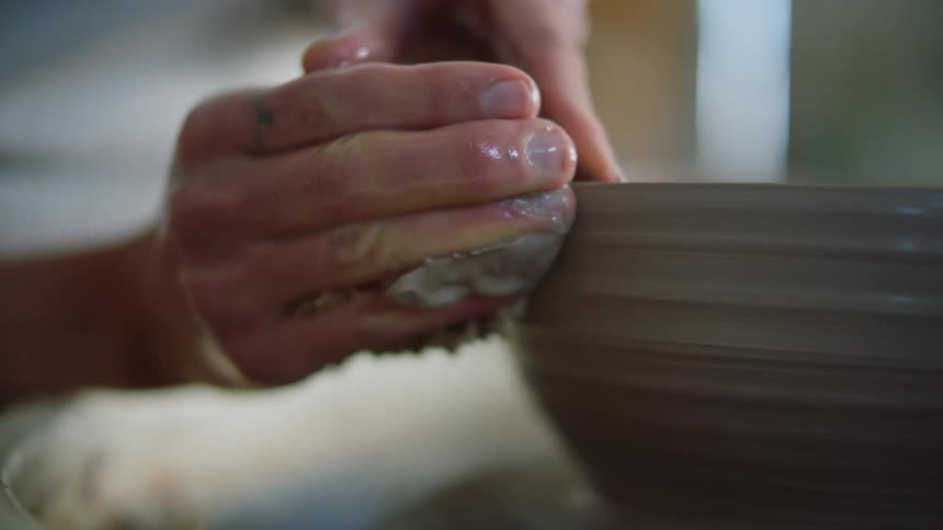Female potter shapes bowl turning on pottery wheel with a sponge