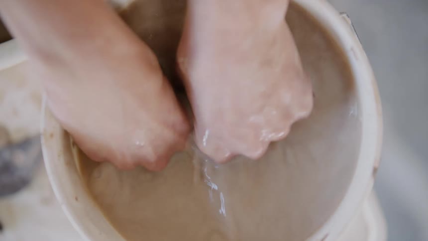 A womans hands being placed inside a bucket of dirty clay water