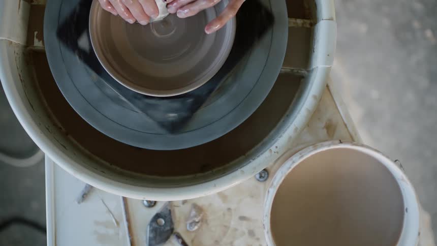 A woman puts water on a tool to shave clay