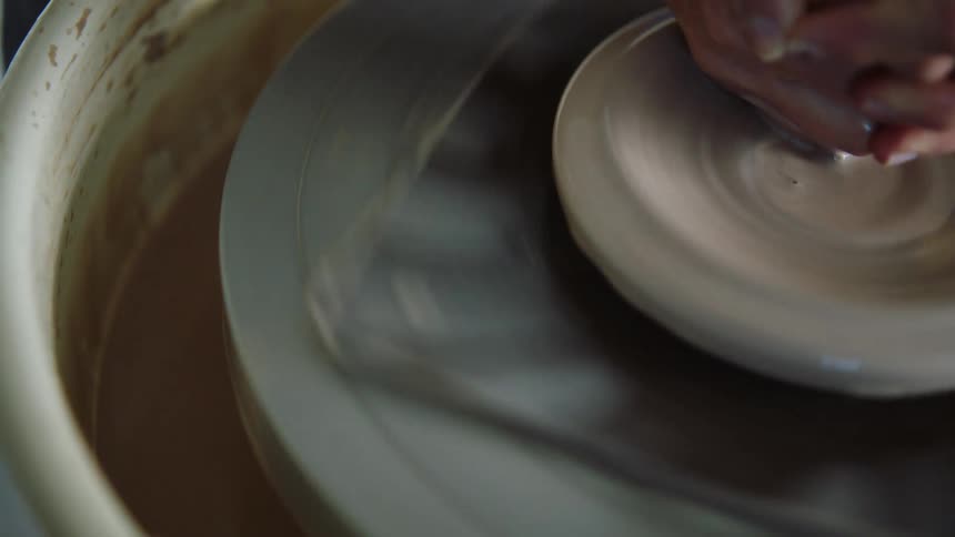 A person holding a clay material that is on a plate rotating to make a specific shape