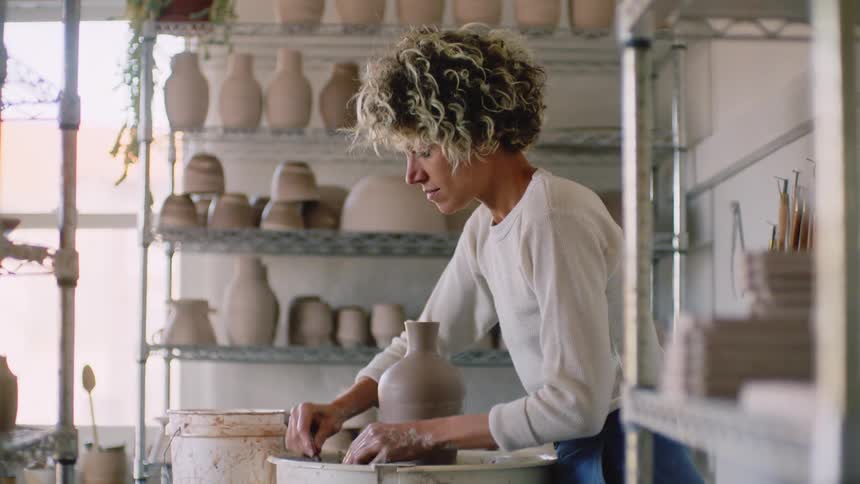 A white woman places a new piece of pottery on a shelf
