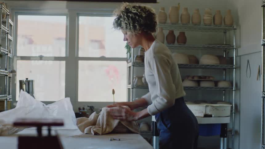 A standing woman takes a cloth and places it on top of an object and then takes it off