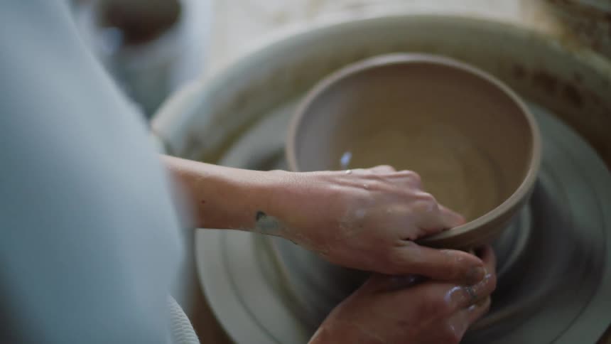 A person finishing shaping a clay bowl
