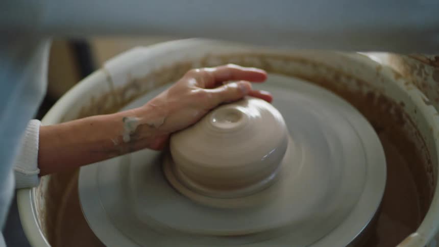 Female potter hits clay she placed on pottery wheel then begins to shape it