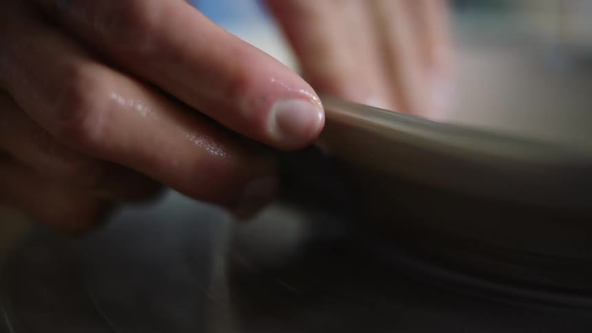 Hands of a woman carefully sculpting the side of a vase in clay