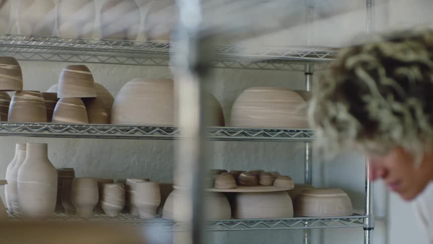 A woman in a room with clay pots in a cupboard