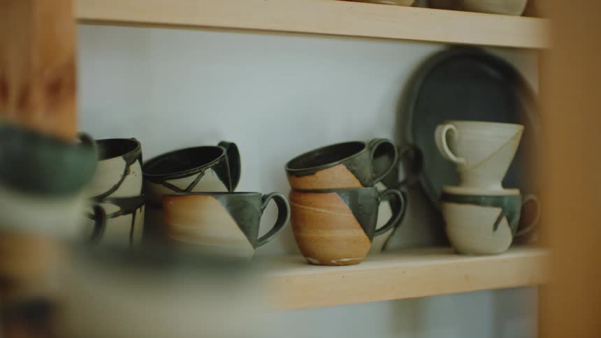 A person takes some clay mugs from a shelf and swaps them around