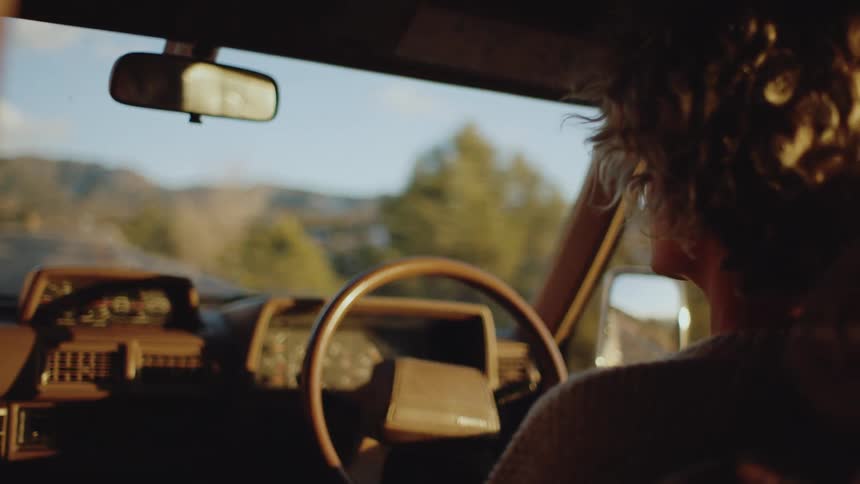A white woman drives a car down a road near mountains