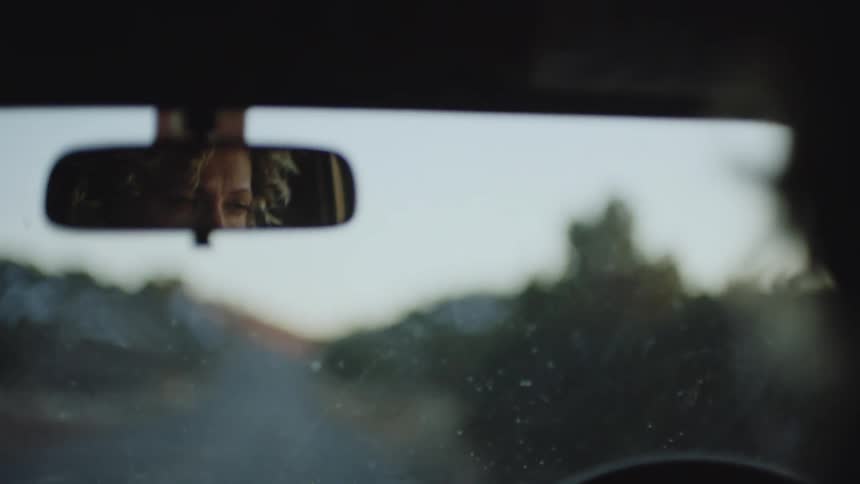 View from inside the car of a woman driving on a road next to nature