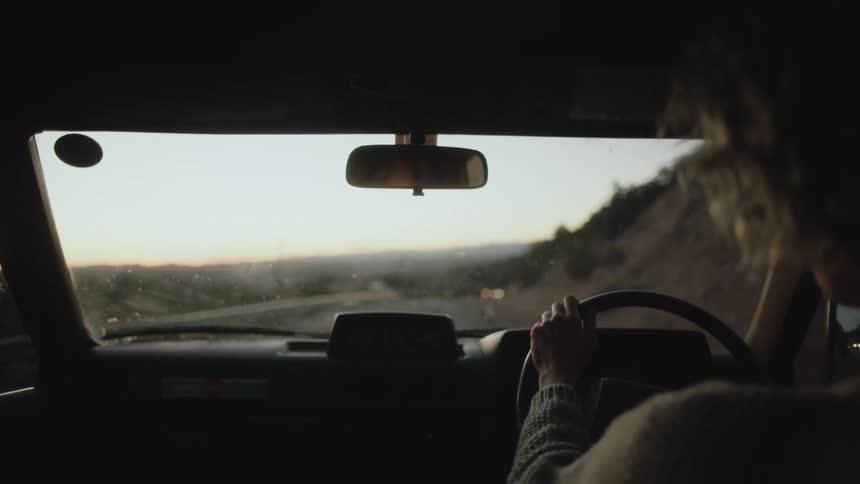 View from inside a womans car driving down a road next to mountains