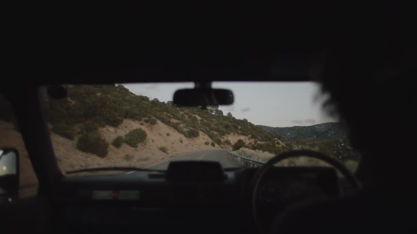 Inside the car a woman driving along a simple road next to mountains
