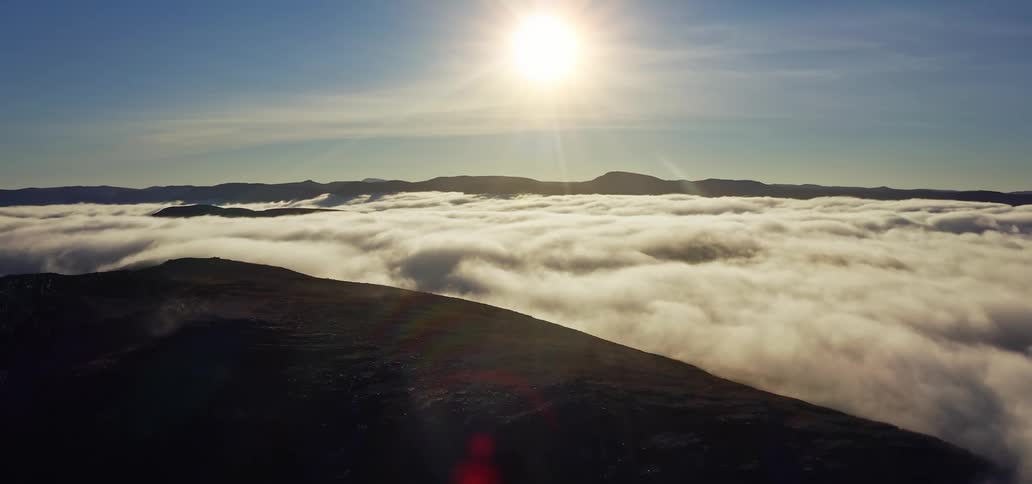 Sun shines brightly onto mountainous landscape partially covered by low lying clouds