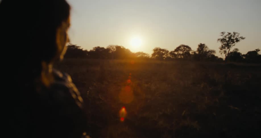 Woman standing in field looks toward the sun glaring from the horizon