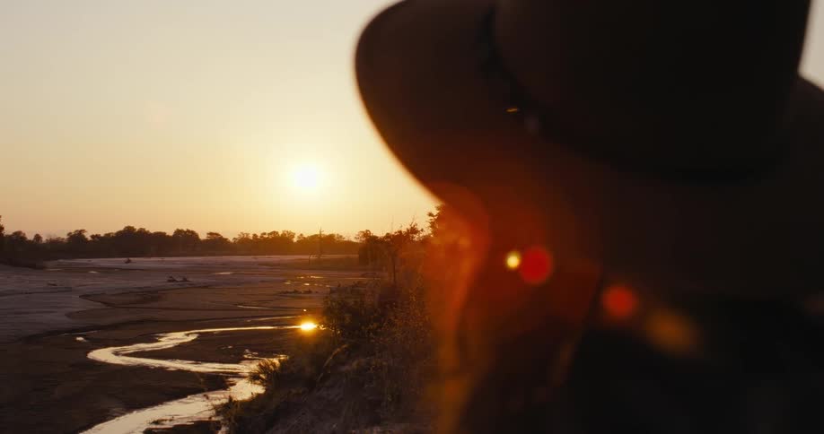 A woman turns her head to look out over a flat terrain ringed by trees