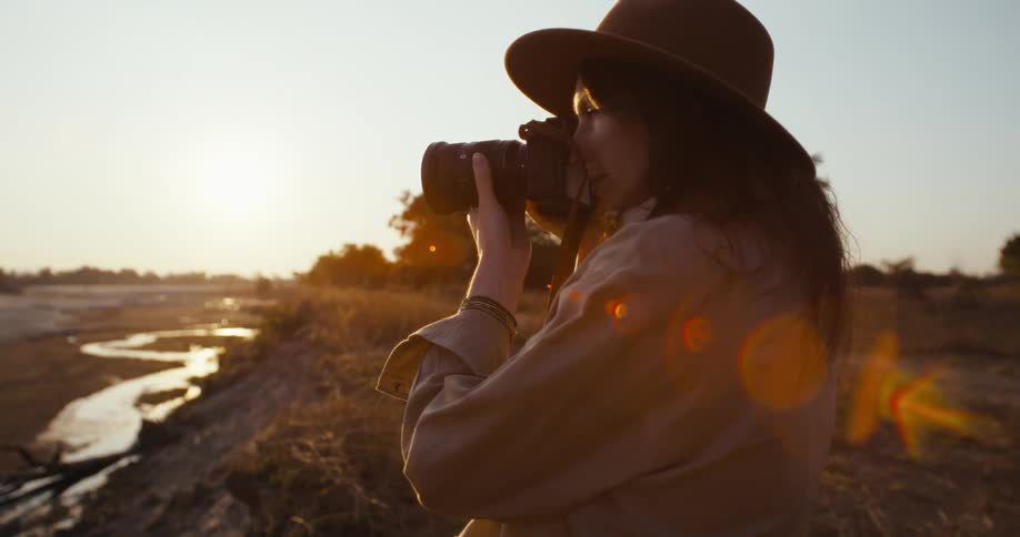 A woman photographing a river in the savannah at sunset