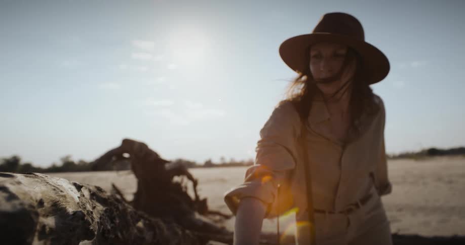 A woman in the desert touches a fallen dead and dry tree trunk then looks around