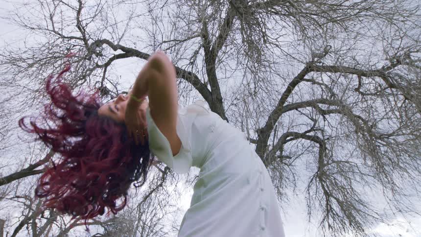 A young woman is dancing outdoors on a cloudy day