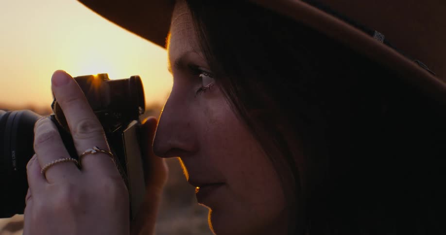 Side portrait of a woman photographer using a professional camera in a natural environment with sun reflection on the horizon