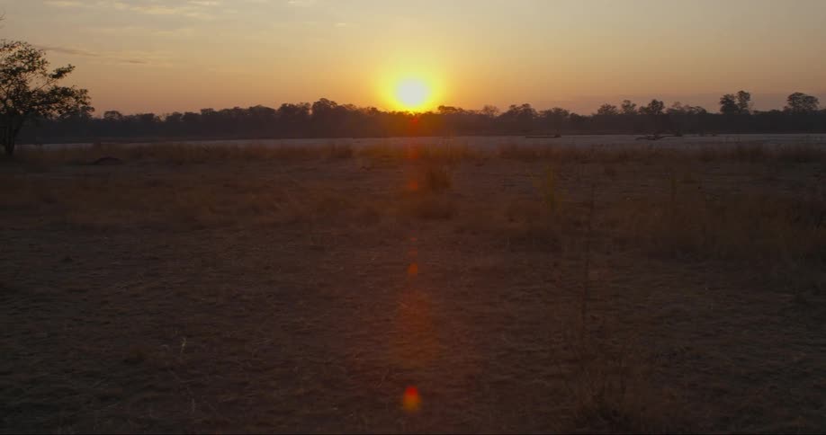 Landscape of a pasture by a lake with the sun on the horizon in a reddish sky