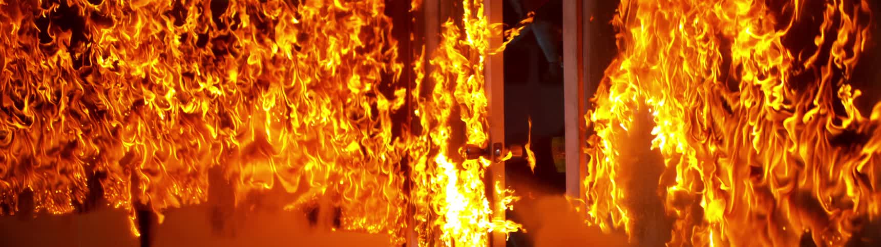 A firefighter is entering a burning building surrounded by intense flames