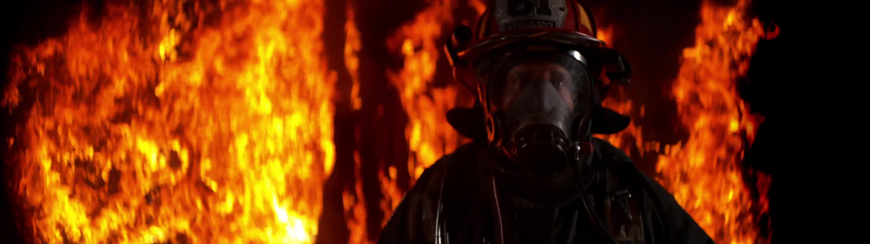A firefighter wearing a mask and helmet walks away from flames burning