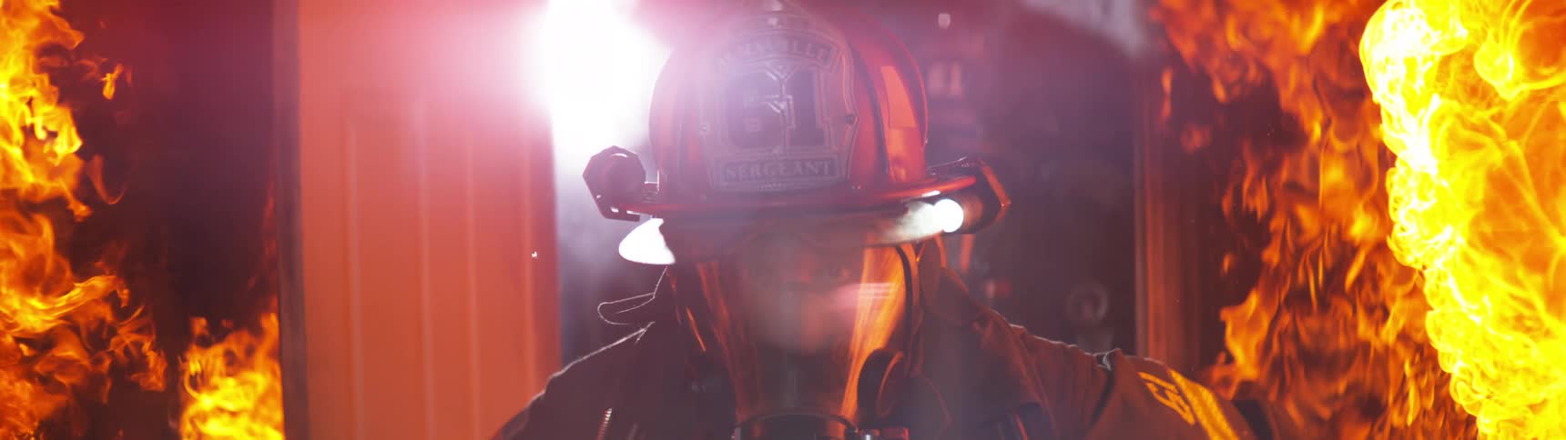 Two firefighters wearing protective helmets entering a residence with fire