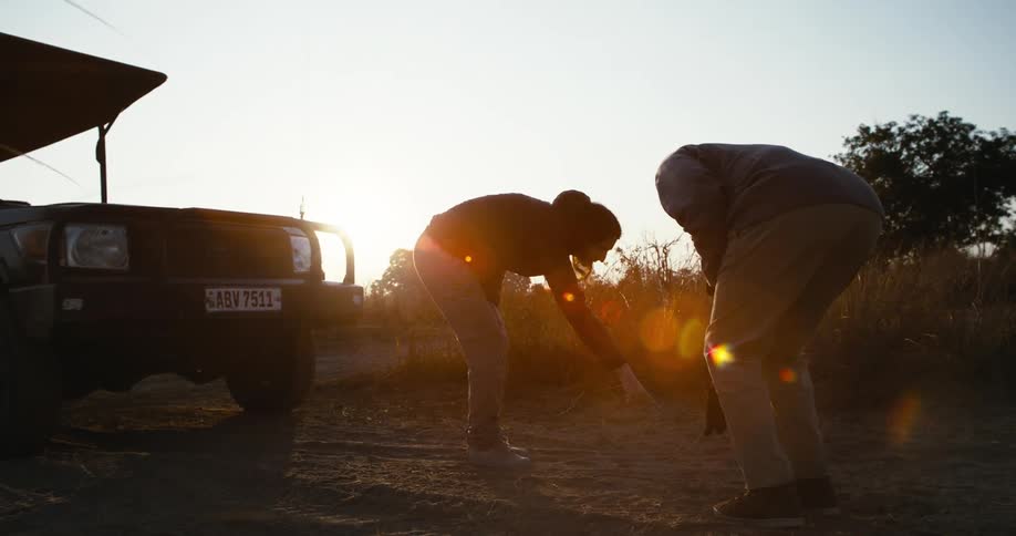 Two people near parked vehicle examine area of dirt road