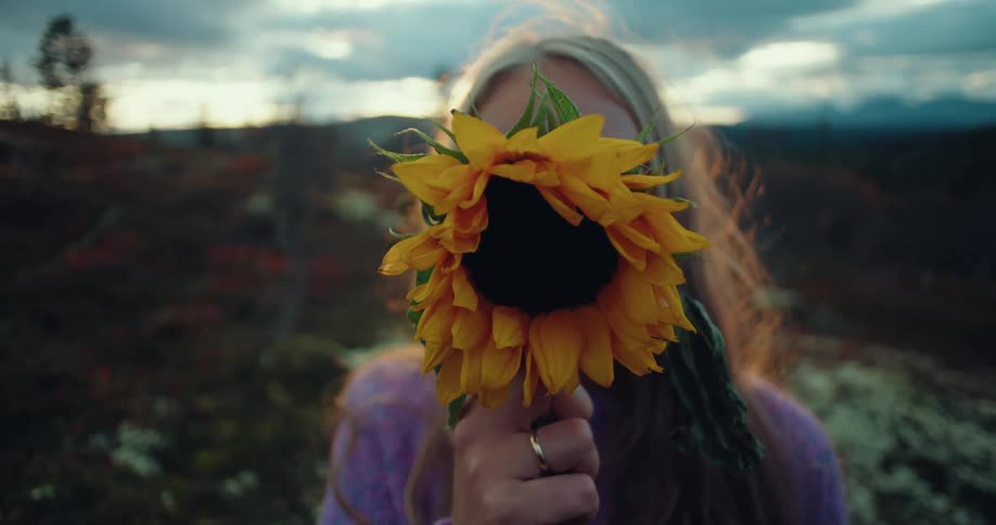 Close up of a woman hiding her face behind a sunflower
