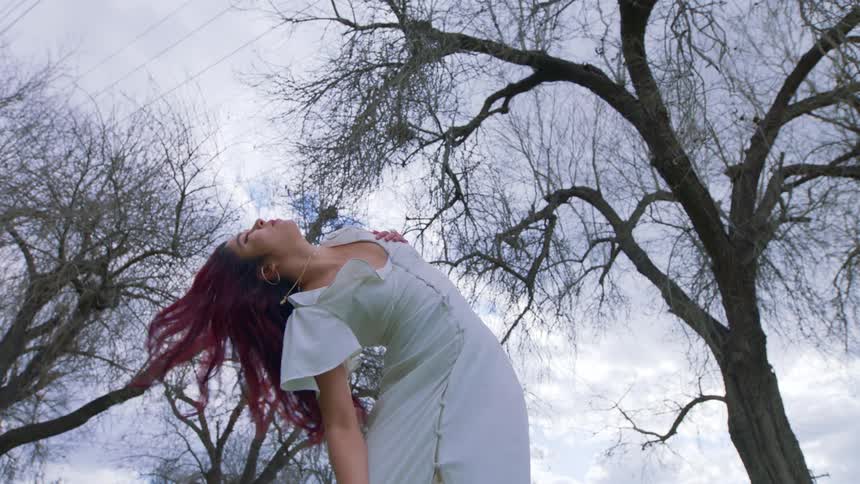 A woman dancing in a park during a cloudy sunset