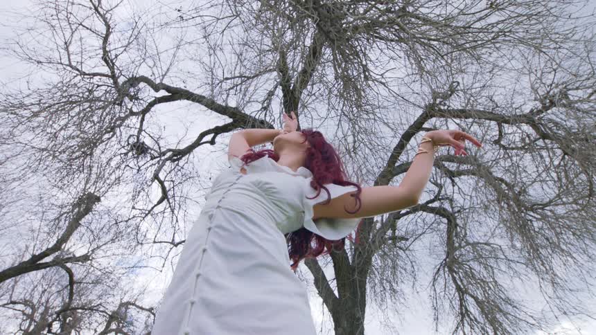 Lady in white gown dancing under a withered tree at midday