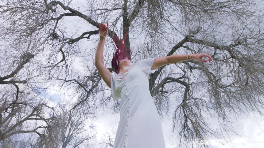 A woman rises and dances in front of a large tree