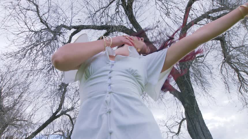 A woman swings her head and arms around while dancing outdoors under a tree