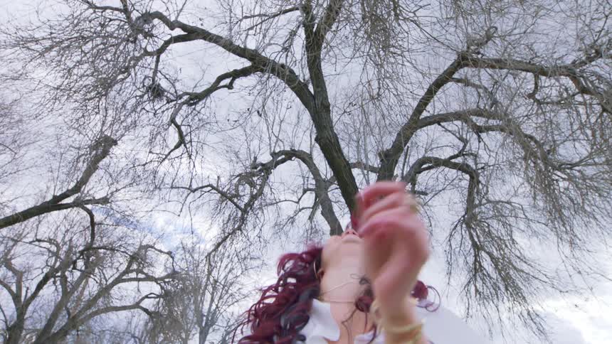 A young woman with long dark hair smiles and jumps while dancing outdoors