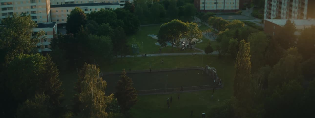 A park with a playground and people surrounded by buildings in the evening light