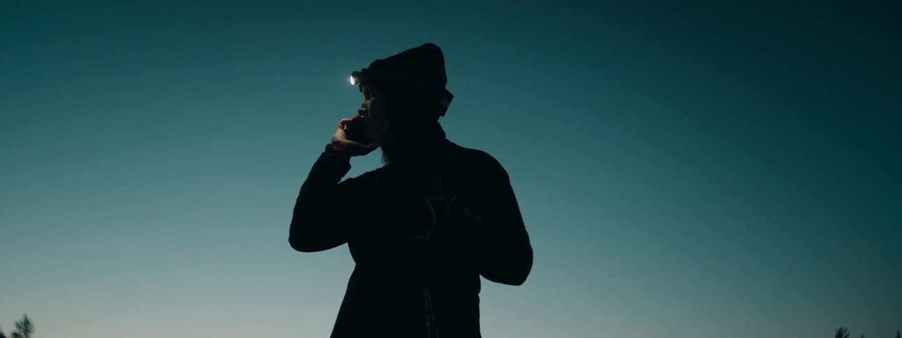 Woman wearing a headlamp while skiing makes a phone call