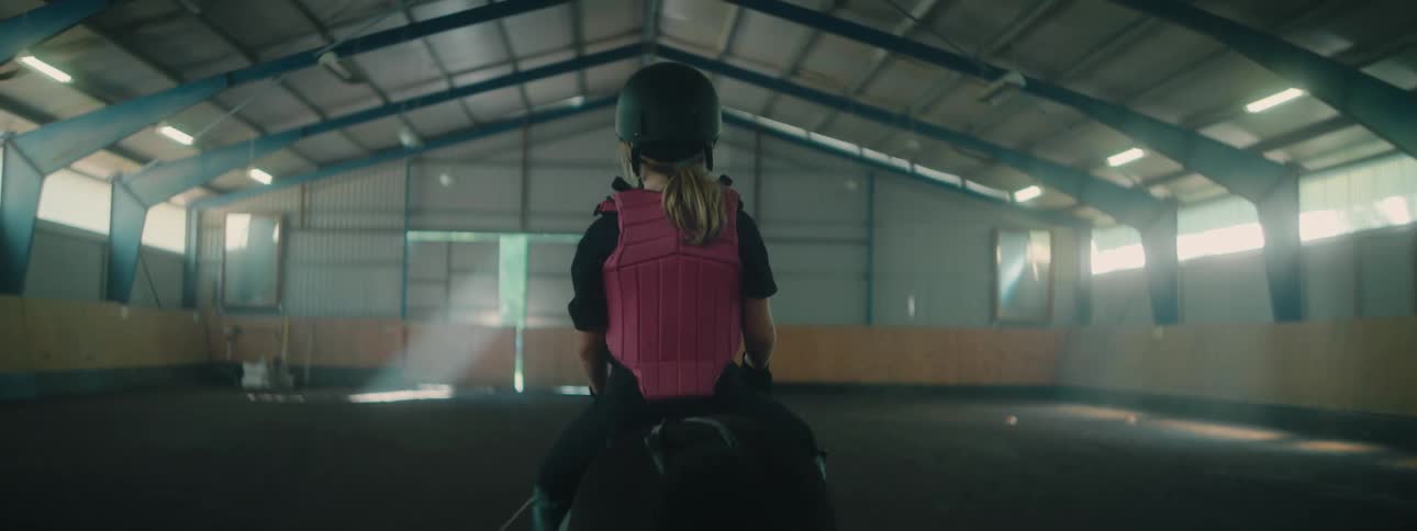 Back view of a young little girl riding a horse indoors