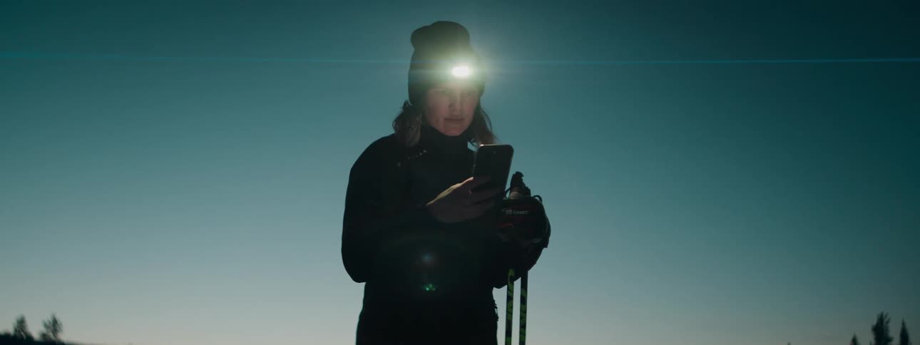Woman on a mountain picking up her cell phone while her flashlight is on at the dawn of the day