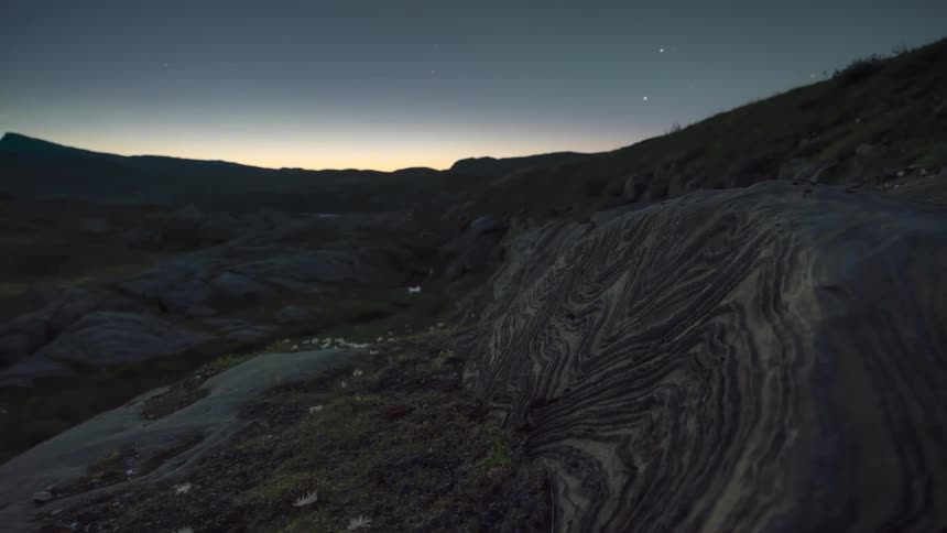 Layered rocks in a volcanic icelandic valley with northern lights in the background as the sun sets into night