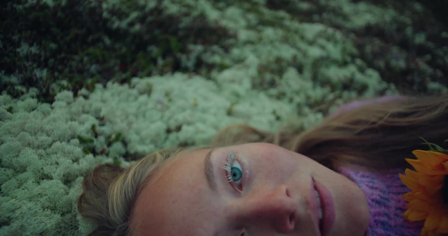 A young woman lying on a mossy rock holding a flower
