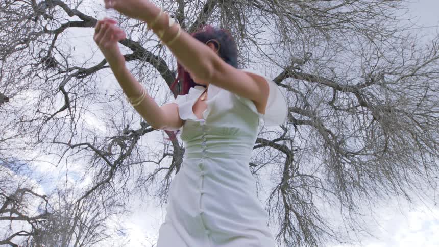 Female dancer wearing white dress swings her auburn hair under a leafless tree on a cloudy day